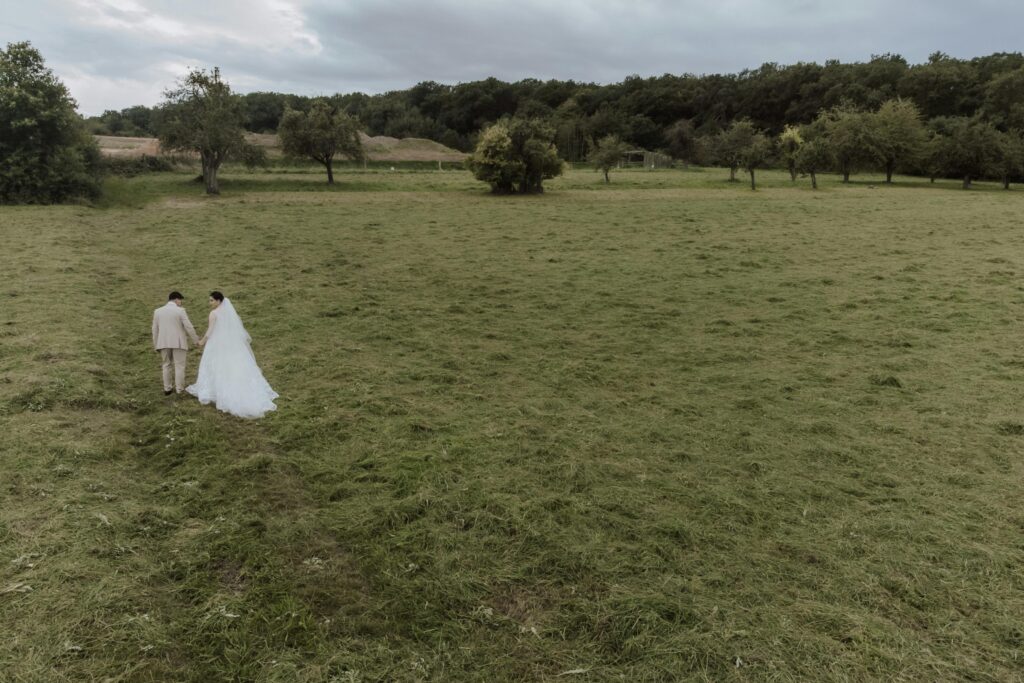 Aerial view of newlywed couple walking through a serene countryside setting.